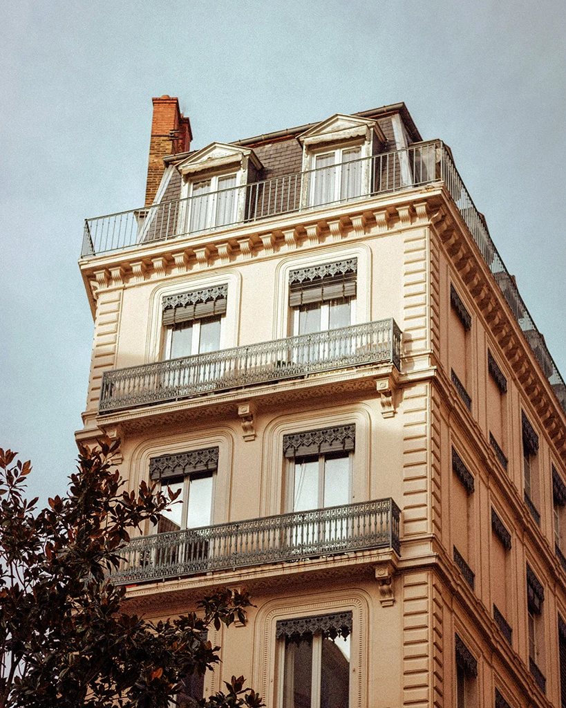 Façade d’un immeuble haussmannien typique à Lyon, avec balcons en fer forgé et fenêtres à encadrement décoratif